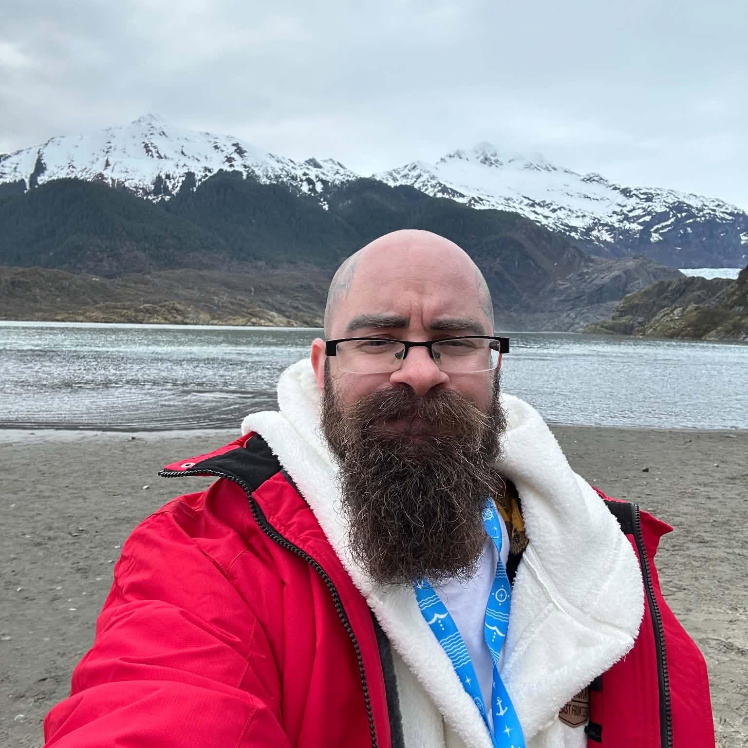 Kaden outdoors in a red jacket, with snowy mountains behind him
